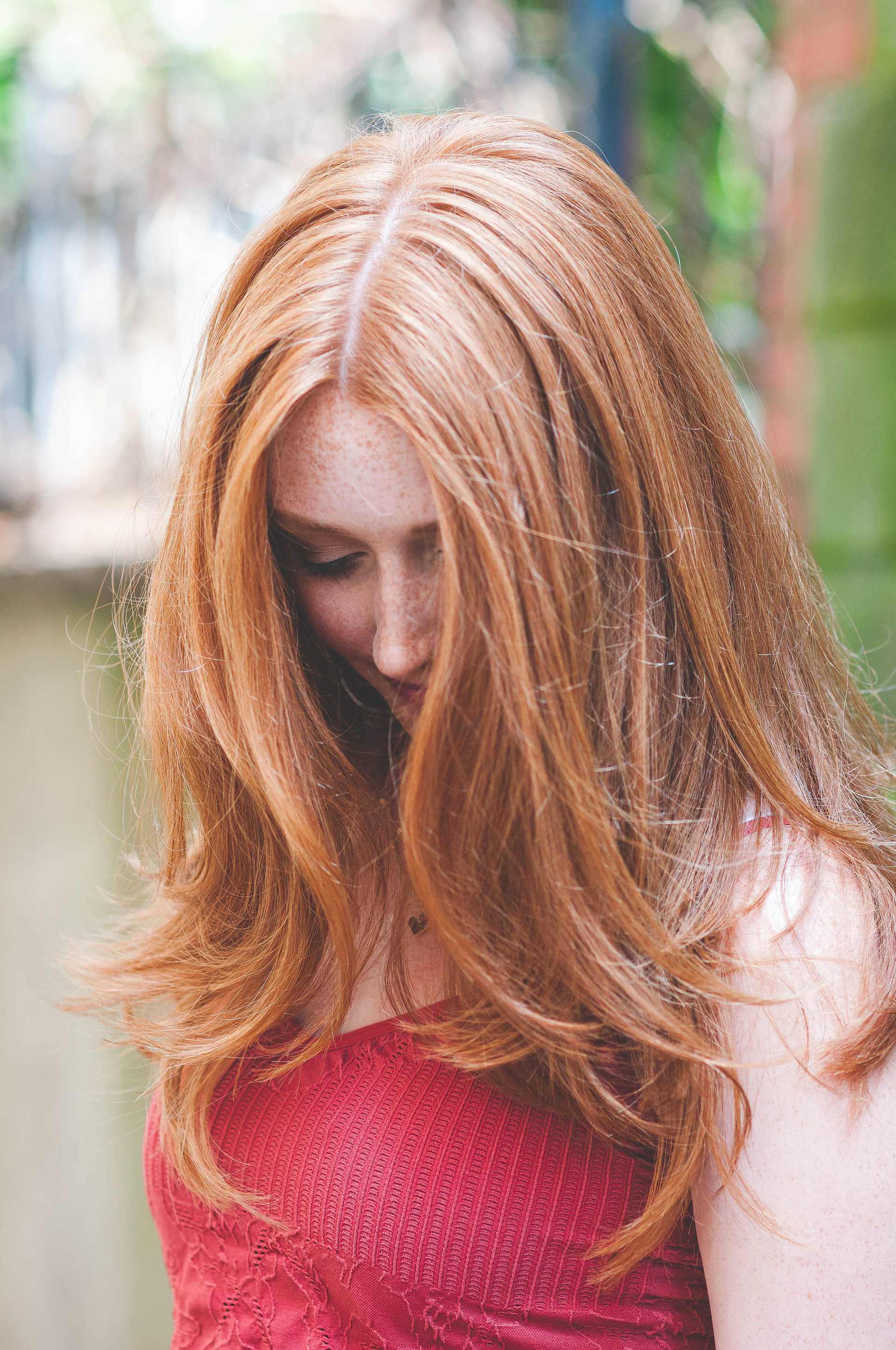 Red-haired woman in red top looking down, outdoors.